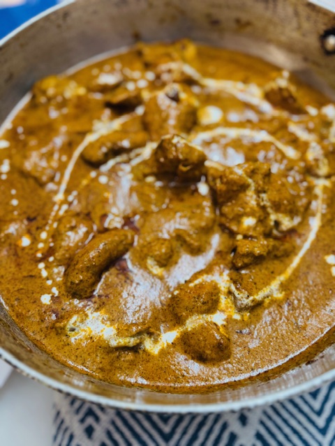 Butter chicken in a copper karahi with fresh cilantro